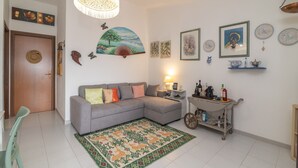 Una sala de estar con un sofá seccional gris, un tapete estampado, un ventilador de pared y un carrito con botellas.