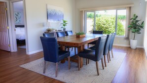 Un comedor con mesa de madera y sillas azules, una planta en maceta y un cuadro en la pared.