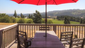 Una terraza de madera con una mesa y sillas, una sombrilla roja y una vista panorámica de un paisaje montañoso.
