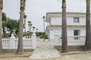 A white building with a tiled roof, surrounded by palm trees and a white fence.