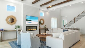 A modern living room with a fireplace, white sofas, a coffee table, and a staircase. - NEW! Luxe Escape w/ Pool & Spa - Close to Beach (Naples)