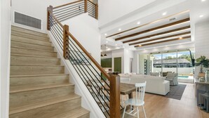 A modern interior with a wooden staircase, white walls, and a dining area with a white table and chairs. - NEW! Luxe Escape w/ Pool & Spa - Close to Beach (Naples)