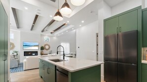 A modern kitchen with a central island, green cabinetry, and a large refrigerator. - NEW! Luxe Escape w/ Pool & Spa - Close to Beach (Naples)