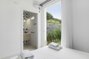 A bedroom with a bed, a bathroom with a shower, and a view of greenery outside.
