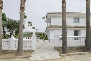 A white building with a tiled roof, surrounded by palm trees and a white fence.