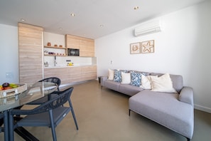 A modern living space with a dining area, a grey sofa, and a kitchen with wooden cabinets. - Vacation 'Kay Lava' with Mountain View, Wi-Fi and Air Conditioning (Caleta de Famara)