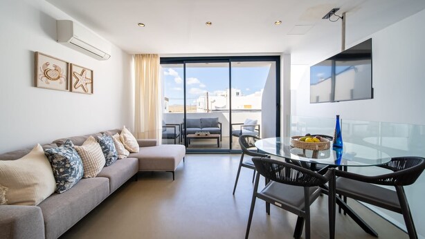 A modern living room with a sofa, dining table, chairs, and a large window.