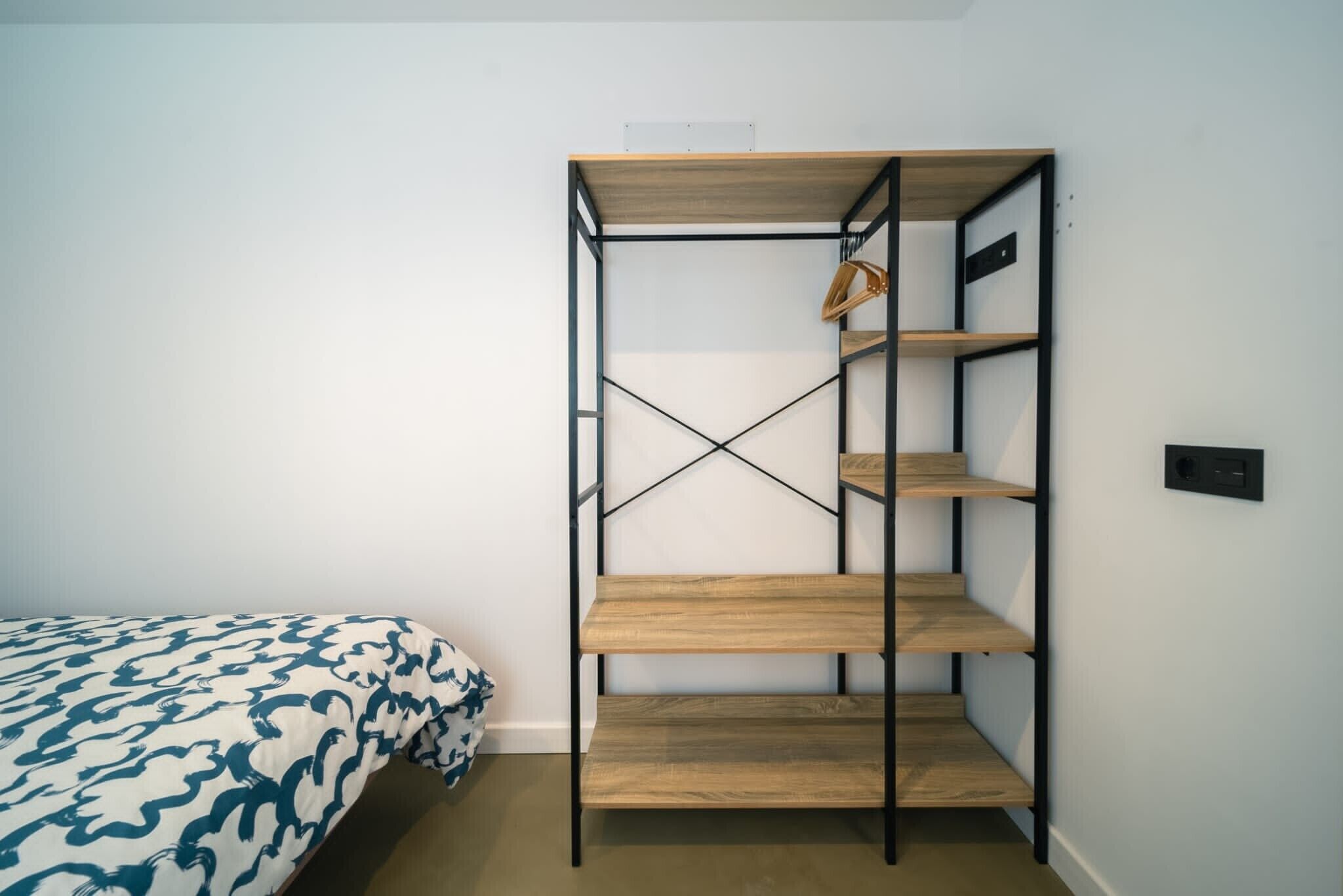 Una cama litera con una colcha estampada, un estante de madera con una cesta colgante y un enchufe en la pared.