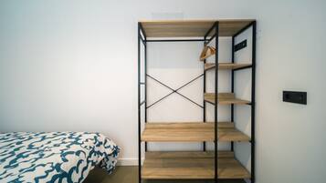 Una cama litera con una colcha estampada, un estante de madera con una cesta colgante y un enchufe en la pared.