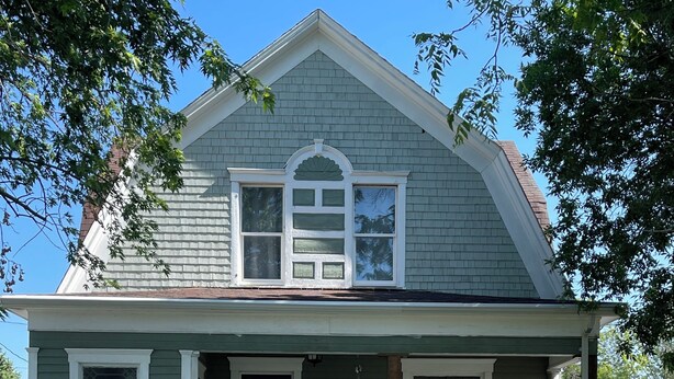 Une maison à deux étages avec un porche à l’avant et une clôture en bois peinte en blanc.