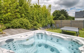 A hot tub in a backyard with a wooden deck, a table, and chairs. - Holiday Home 'An Alré - Piscine - Spa - Ciné' with Private Pool, Private Terrace and Wi-Fi (Brech)