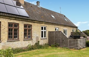 A traditional brick house with large windows, a sloped roof, and a wooden fence.