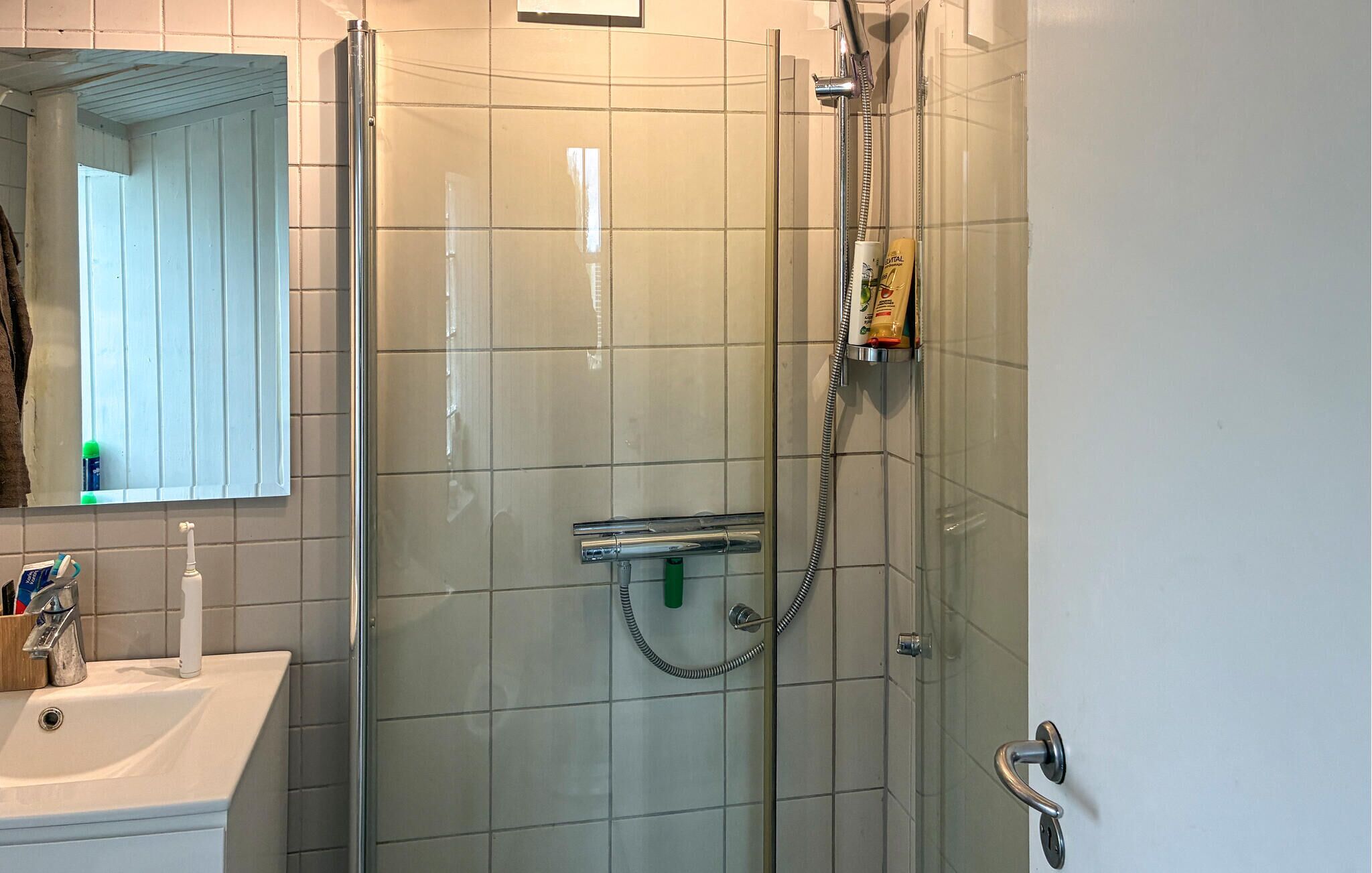 Un baño con ducha de vidrio, un lavamanos blanco y un espejo.
