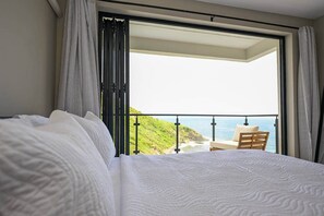 A bedroom with a bed, a balcony with a view of the ocean, and a chair. - Villa Jasiri (Gros Islet)