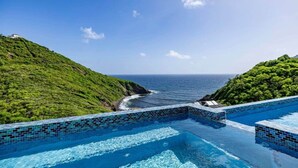 Una piscina infinita con vista al océano y colinas verdes.