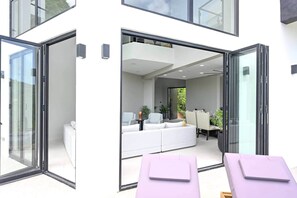 A modern interior with a white sofa, a dining table, and a glass door leading outside.
