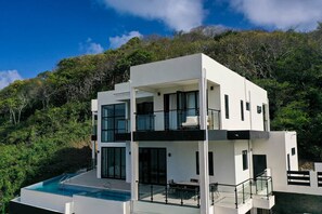 A modern two-story house with a swimming pool, large windows, and a balcony.