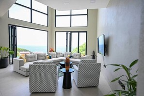 A modern living room with a large sectional sofa, patterned armchairs, a coffee table, and a TV mounted on the wall. - Villa Jasiri (Gros Islet)