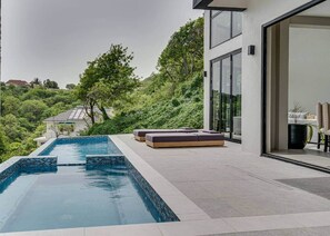 A modern outdoor pool area with a built-in seating area and a view of a lush green landscape. - Villa Jasiri (Gros Islet)