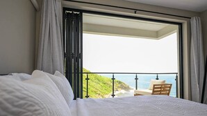 Un dormitorio con una cama, un balcón con vista al océano y una silla.