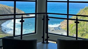 Una habitación con amplios ventanales que ofrecen vista al océano y a un paisaje montañoso.