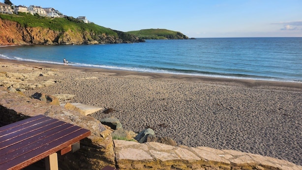 Una spiaggia di ciottoli con una panchina di legno e un muro in pietra.
