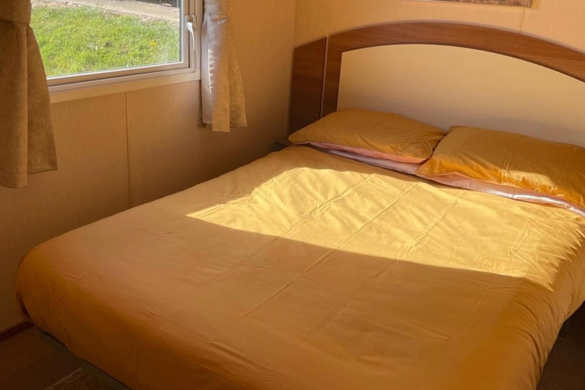 A bed with a wooden headboard, a yellow bedspread, and a window with curtains.