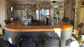 A bar area with a counter, chairs, a refrigerator, and a wall with pictures. - Royal Hotel (Yeoval)