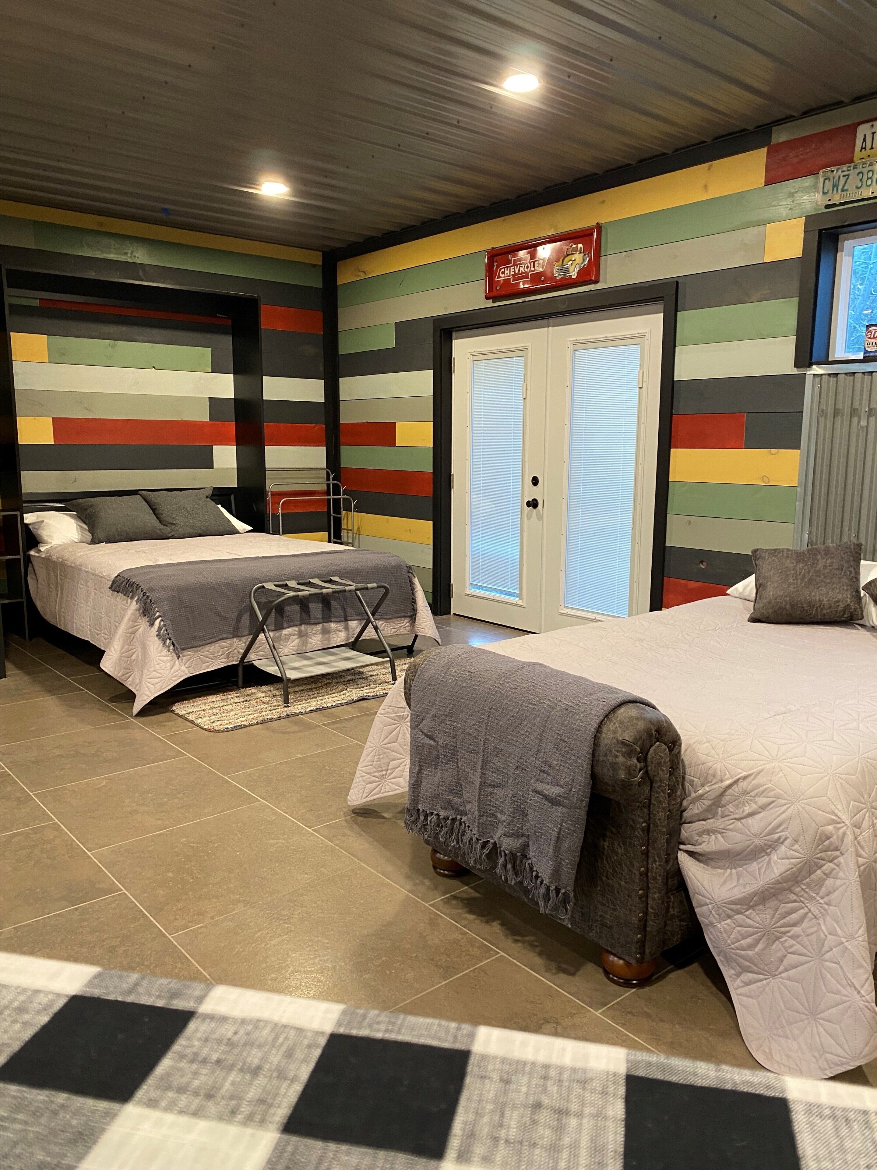 A bedroom with two beds, a colorful striped wall, a Chevrolet sign, and a door with a window.
