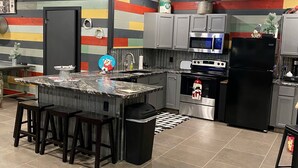 A modern kitchen with a central island, grey cabinets, stainless steel appliances, and a colorful striped wall.