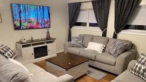 Een woonkamer met een grijze bank, een salontafel, een televisie aan de muur en een open haard.