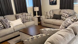 Een moderne woonkamer met twee grijze banken, decoratieve kussens, een houten salontafel en een vloerlamp.