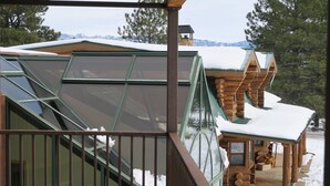 A cabin with a glass-enclosed staircase, wooden exterior, and a snow-covered roof. - Pine Grove Estate: Beautiful Log home on 40 acres with fantastic Mountain Views (Ridgway)