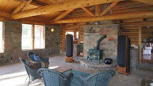 A log cabin interior with stone walls, a stone fireplace, wicker furniture, and a wooden ceiling. - Pine Grove Estate: Beautiful Log home on 40 acres with fantastic Mountain Views (Ridgway)