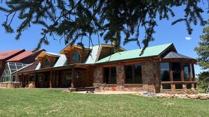 A log cabin with a stone foundation, large windows, and a green roof. - Pine Grove Estate: Beautiful Log home on 40 acres with fantastic Mountain Views (Ridgway)