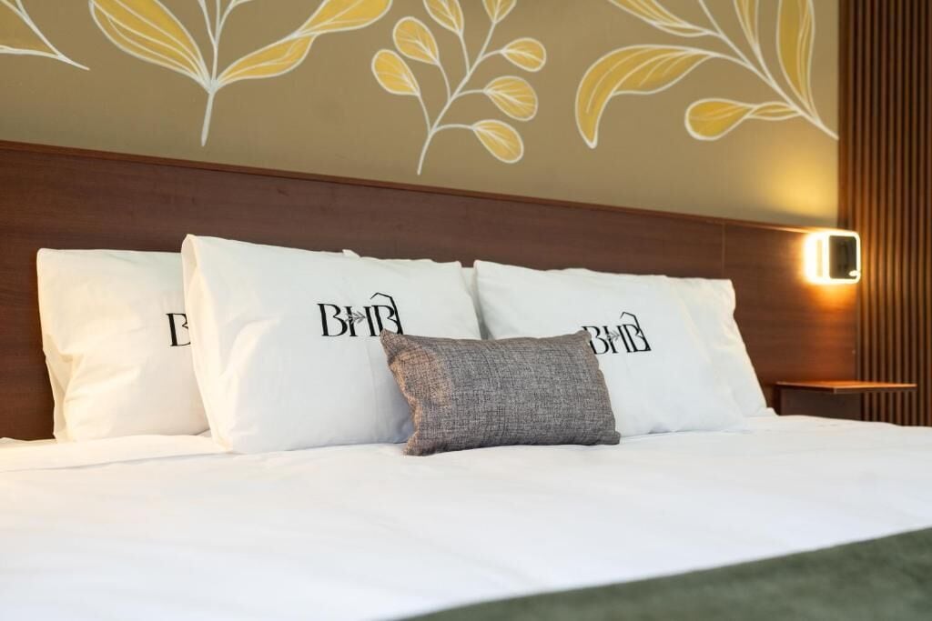 Un lit bien fait, avec une literie et des oreillers blancs, dont l’un porte le logo « B&B ».