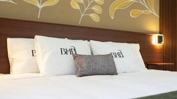 Un lit bien fait, avec une literie et des oreillers blancs, dont l’un porte le logo « B&B ».