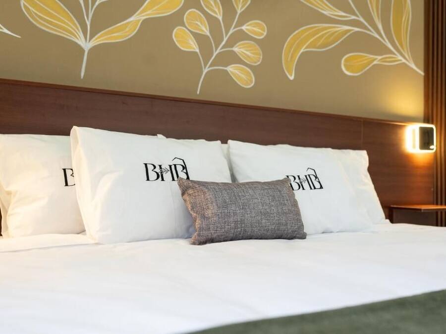 Un lit bien fait, avec une literie et des oreillers blancs, dont l’un porte le logo « B&B ».