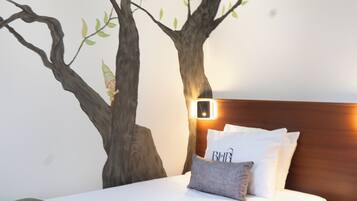 A bedroom with a bed, a nightstand, a wall-mounted lamp, and a tree mural.