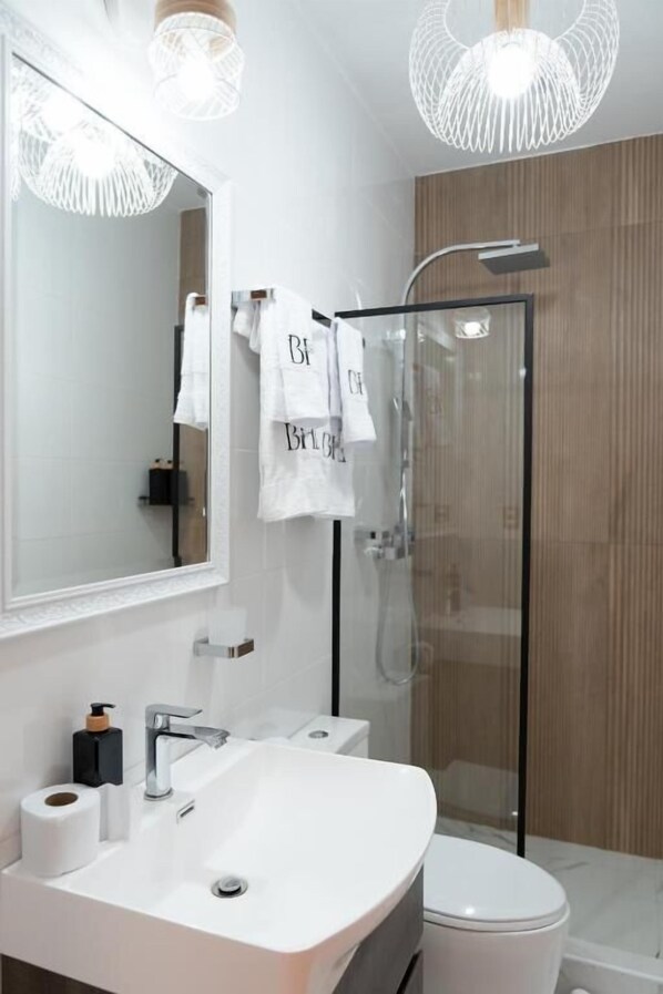 A modern bathroom with a large mirror, a white sink, a toilet, and a glass-enclosed shower.
