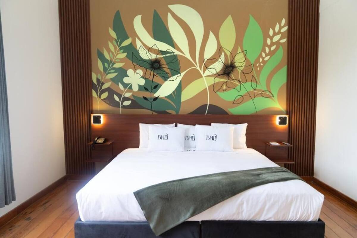 A hotel room with a large bed, a wooden headboard, and a wall mural with floral designs.