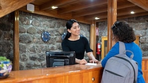 A reception desk with a stone wall background, a clock, and a fire extinguisher. - Bosco Hotel Boutique (Cusco)