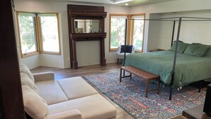 Un dormitorio con cama, banca, sofá, chimenea y ventanas grandes.
