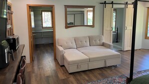 Una sala moderna con un sofá color beige, una cafetera, un televisor y un espejo grande.