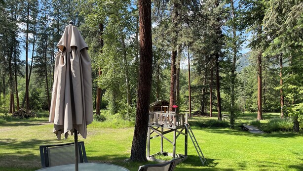 Una terraza de madera con una mesa y sillas de vidrio, rodeada de un bosque.