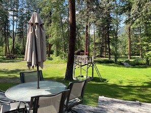 A wooden deck with a glass table and chairs, surrounded by a forest. - Relax and unwind while taking in nature at this master suite on 5 acres! (Frenchtown)
