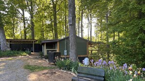 A rustic cabin with a wooden exterior, surrounded by a gravel path and lush greenery.
