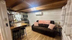 A compact living space with a kitchenette, a sofa, a dining table, and a bar stool.