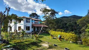 Une maison blanche avec un toit rouge, entourée d’un jardin luxuriant et verdoyant, et située dans un paysage vallonné.