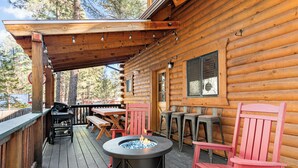 A wooden deck with a fire pit, outdoor seating, and a covered area.